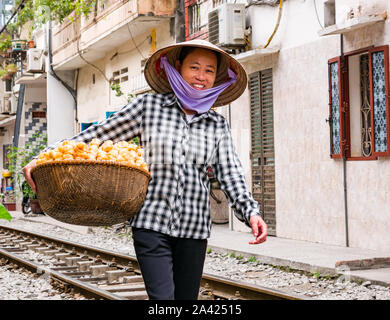 Smiling Asian women, food street vendeur vietnamien portant chapeau conique, marcher sur les voies de chemin de fer dans le village ou en train Street, Hanoi, Vietnam Banque D'Images