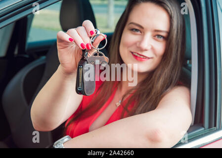 L'accent en forme de voiture avec trousseau clés sur l'arrière-plan d'heureux succès femme assise dans sa nouvelle voiture. Voir l'extérieur. Selective focus, copy space Banque D'Images