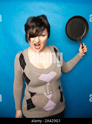 Femme de battre avec une poêle à fond bluw studio seul. Banque D'Images