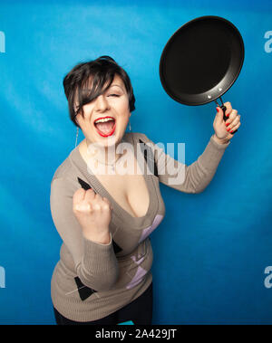 Femme de battre avec une poêle à fond bluw studio seul. Banque D'Images