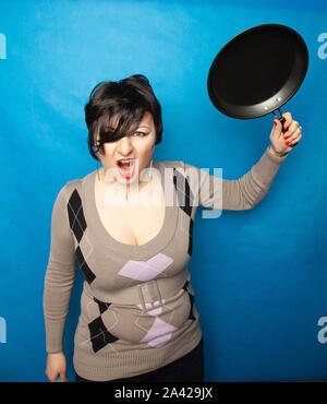 Femme de battre avec une poêle à fond bluw studio seul. Banque D'Images