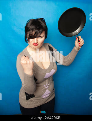 Femme de battre avec une poêle à fond bluw studio seul. Banque D'Images