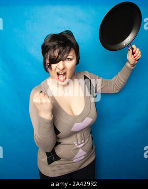 Femme de battre avec une poêle à fond bluw studio seul. Banque D'Images