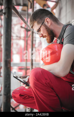 Site de construction worker sitting haut sur l'échafaudage, le repos et l'aide de mobile phone Banque D'Images