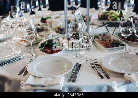 Vue sur table mariage nappe blanche avec couverts de verres vides, assiettes et ustensiles. Des collations sont servies sur la table. Banque D'Images