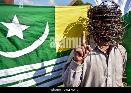 Un manifestant avec du fil de fer barbelé autour de sa tête fait un geste devant un drapeau pendant la manifestation.Une manifestation a eu lieu à Srinagar, ville peu après la prière du vendredi à la suite de la suppression de l'article 370 par le gouvernement central qui accorde un statut spécial à Jammu-et-Cachemire. Banque D'Images