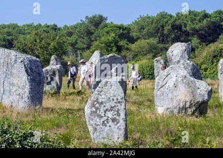 Guide avec personnes âgées touristes marcher parmi les alignements de Ménec, site mégalithique entre les menhirs de Carnac, Morbihan, Bretagne, France Banque D'Images
