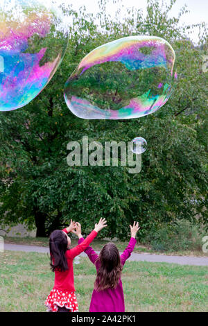 Deux jeunes filles atteignant et tente de prendre des bulles géantes. Banque D'Images