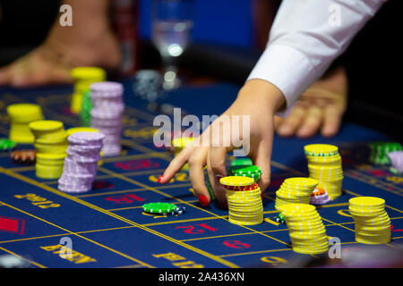 Table de roulette avec des mains de poser des jetons dans un casino. La roue de roulette à l'avant-plan. Jouer jeu. Les gens méconnaissables. Banque D'Images