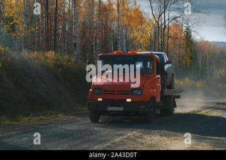 Dépanneuse rides le long d'une route forestière dans le contexte d'une forêt d'automne. L'aide sur les transports routiers wrecker broken voiture. Banque D'Images