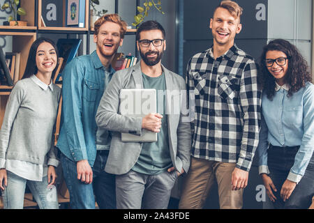 Startupers travailler ensemble au comité permanent du bureau bearded man holding laptop à la joyeuse de l'appareil photo Banque D'Images