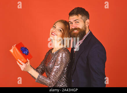 Couple heureux avec boîte cadeau, proches les uns des autres avec le sourire. Modèles de race blanche dans l'amour, relation, dating, flirt amoureux. Concept romantique. L'homme et la femme avec boîte-cadeau isolé sur fond rouge. Banque D'Images