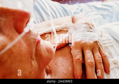 Détail d'un patient de respirer de l'oxygène au moyen d'une canule nasale en plastique et d'une canule intraveineuse insérée dans la main. Banque D'Images