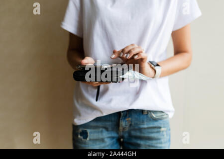 Porte-monnaie avec des dollars américains et du téléphone mobile dans les mains, femme ou paiement en argent shopping concept. Fille sortir l'argent de la bourse de cuir noir à la main, Banque D'Images