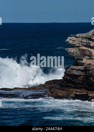 Oceanside falaise de grès rocheux avec de l'eau créant des vagues de la mer bleu camouflage contre Côte et Ciel clair en arrière-plan Banque D'Images