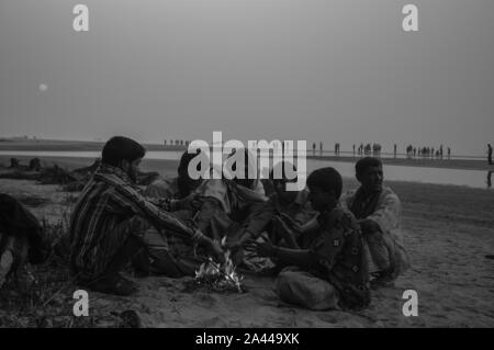 Les personnes à faible revenu se réchauffent à la chaleur de la combustion de déchets dangereux dans un matin d'hiver à Kuakata sea beach. Patuakhali, Bangladesh. Banque D'Images