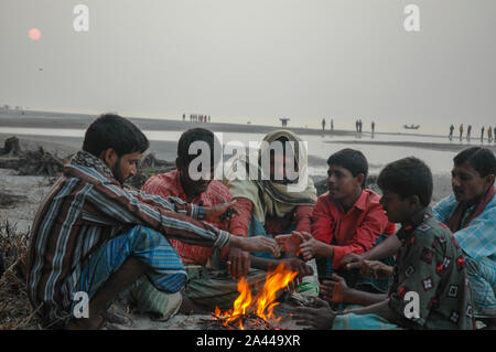 Les personnes à faible revenu se réchauffent à la chaleur de la combustion de déchets dangereux dans un matin d'hiver à Kuakata sea beach. Patuakhali, Bangladesh. Banque D'Images