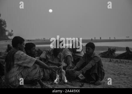 Les personnes à faible revenu se réchauffent à la chaleur de la combustion de déchets dangereux dans un matin d'hiver à Kuakata sea beach. Patuakhali, Bangladesh. Banque D'Images