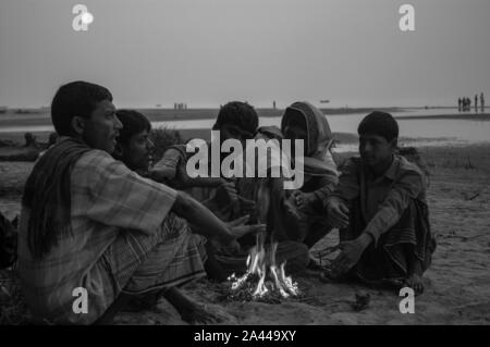 Les personnes à faible revenu se réchauffent à la chaleur de la combustion de déchets dangereux dans un matin d'hiver à Kuakata sea beach. Patuakhali, Bangladesh. Banque D'Images