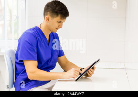 Woman blue coat travaillant sur la ligne avec une tablette dans un dentiste clinique. Banque D'Images