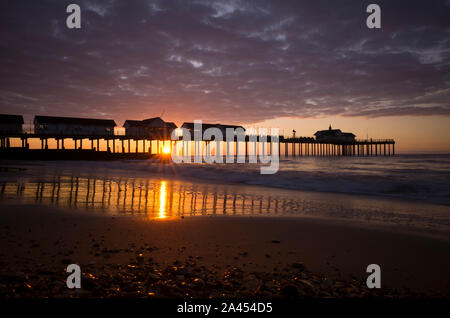 Southwold pier au lever du soleil, prises à partir de la plage déserte à partir d'un point de vue bas avec des cailloux au premier plan. Banque D'Images