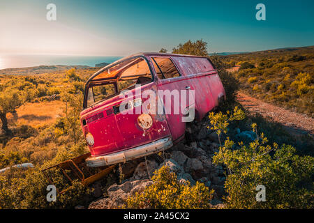 Bus van abandonnés sur des rochers au milieu de nulle part, sur une journée ensoleillée. La mer en arrière-plan. Banque D'Images