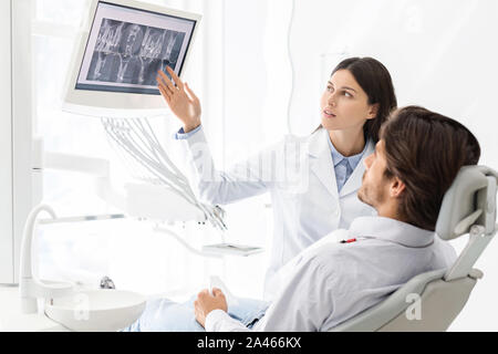 Jolie dentiste médecin démontrant son patient les résultats radiologiques Banque D'Images