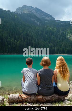 Famille, de la mère avec garçon et fille, reste sur tree log sur le lac Noir (Crno jezero), shore paysage estival. Municipalité de Zabljak, au Monténégro. Banque D'Images