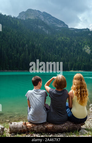 Famille, de la mère avec garçon et fille, reste sur tree log sur le lac Noir (Crno jezero), shore paysage estival. Municipalité de Zabljak, au Monténégro. Banque D'Images