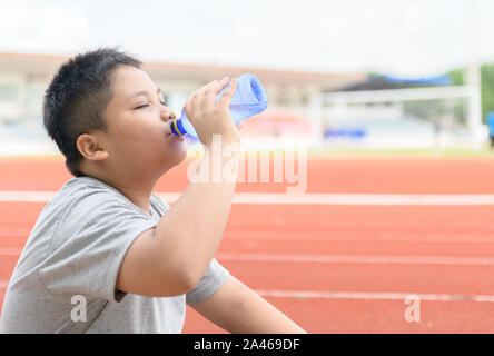 Asian boy Fat boire de l'eau dans une bouteille en plastique à côté d'une piste de course de réduire sa soif. Concept de l'exercice et en bonne santé Banque D'Images