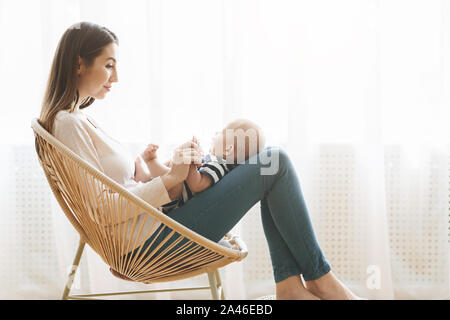 Mère et bébé nouveau-né sur les genoux assis en fauteuil tissé Banque D'Images