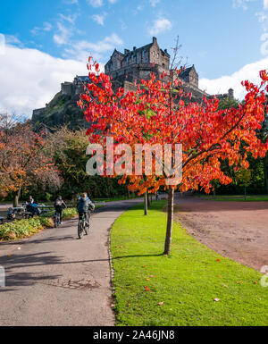 Princes Street Garden, Édimbourg, Écosse, Royaume-Uni, 12 octobre 2019.Météo au Royaume-Uni : les gens d'Édimbourg profitent d'une belle journée d'automne chaude et ensoleillée dans la capitale.Un arbre d'automne orange coloré avec le rocher du château d'Édimbourg tandis que les garçons pédalez à vélo Banque D'Images