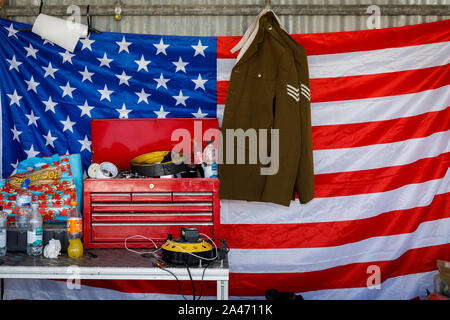 Drapeau américain accroché avec veste militaire et la boîte à outils dans le paddock moto au garage 2019 Goodwood Revival, Sussex, UK. Banque D'Images