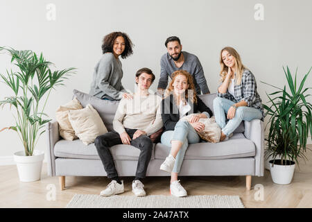 Les adolescents en interculturel joyeuse casualwear relaxing on sofa together Banque D'Images