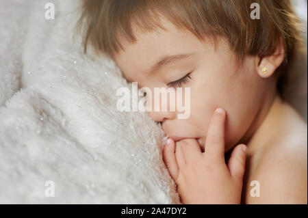 Sucer doigt baby girl sleeping on soft white bed Banque D'Images