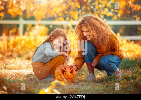 Preparaton Halloween Concept. Mère et fille debout à l'extérieur à jouer avec la citrouille sculptée heureux Banque D'Images