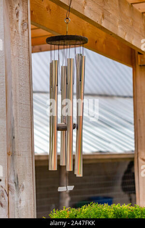 Wind Chimes métalliques sont suspendues à une poutre en bois, partie d'un pavillon extérieur dans un jardin. Banque D'Images