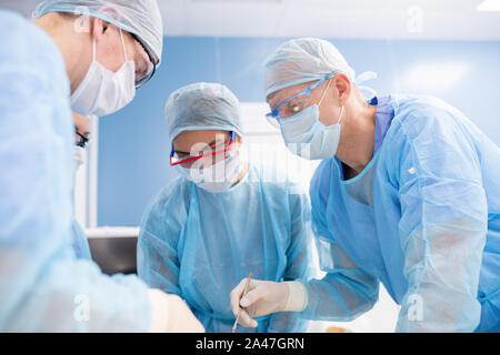 Groupe de chirurgiens en masques, gants et vêtements de se plier plus patient Banque D'Images