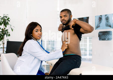 Jolie jeune femme africaine doctor examining patient African man with stethoscope in medical office Banque D'Images