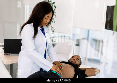 Malade et mal de ventre homme africain en cours d'examen par la femme médecin. Docteur en appuyant sur le ventre de son patient, contrôle du domaine de la douleur Banque D'Images