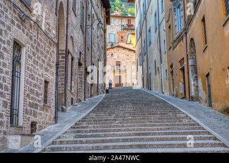Assisi, Italie - 12 août, 2019 : Senior citizen nettoie en face d'une maison dans une ruelle dans la ville Banque D'Images