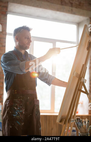 Homme sérieux painter holding paintbrush pendant le travail en face de chevalet Banque D'Images