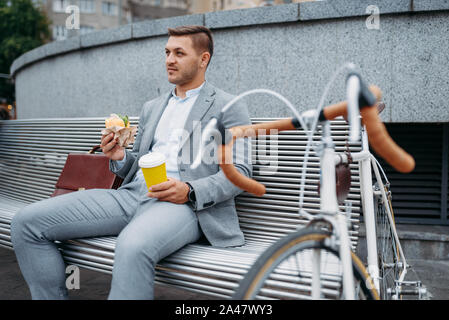 Cycle d'affaires avec mange à midi sur le banc Banque D'Images
