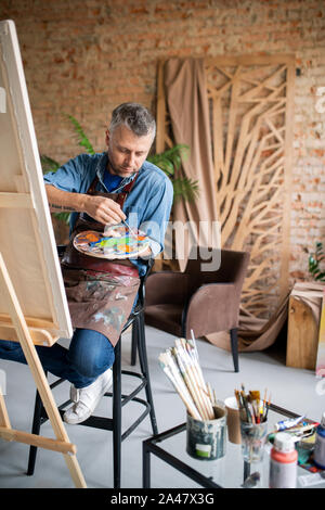 Peintre contemporain casualwear et un tablier en mélangeant les couleurs sur la palette Banque D'Images