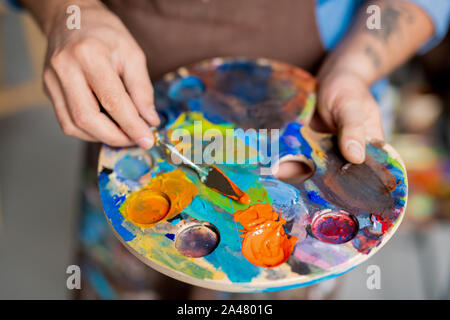 La main du peintre mélange des peintures sur palette avec petit instrument avant peinture Banque D'Images