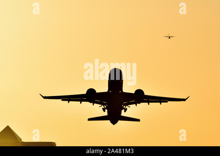 Avion au décollage de l'aéroport de London City avec un ciel d'or que le soleil se couche derrière les toits de Canary Wharf Banque D'Images