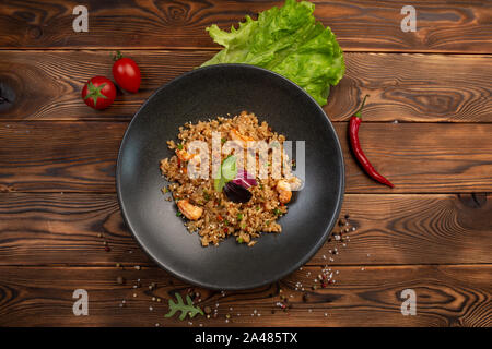 Ebi chahan japonais frit riz aux légumes, les crevettes et la sauce soja dans une plaque noire sur un fond de bois Banque D'Images