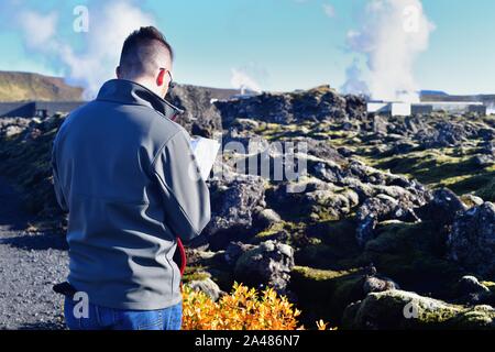 Svartsengi, Islande. Un homme d'accéder à un guide touristique sur les roches entourant le Lagon Bleu L'une des principales attractions touristiques. Banque D'Images