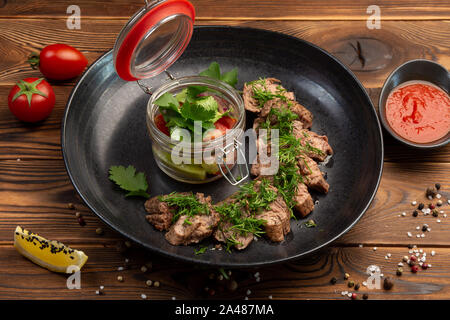 Émincé de veau de machette steak steak avec une salade fraîche et sauce épicée dans une plaque noire sur un fond de bois Banque D'Images