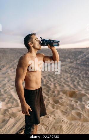 L'athlète masculin de l'eau boissons après entraînement in desert Banque D'Images